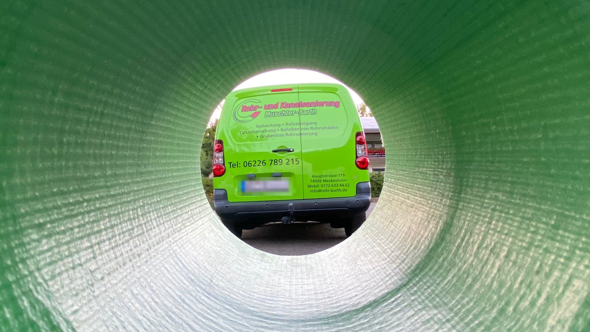 Blick durch ein grünes Rohr auf den beschrifteten Firmenwagen von Muschter-Barth