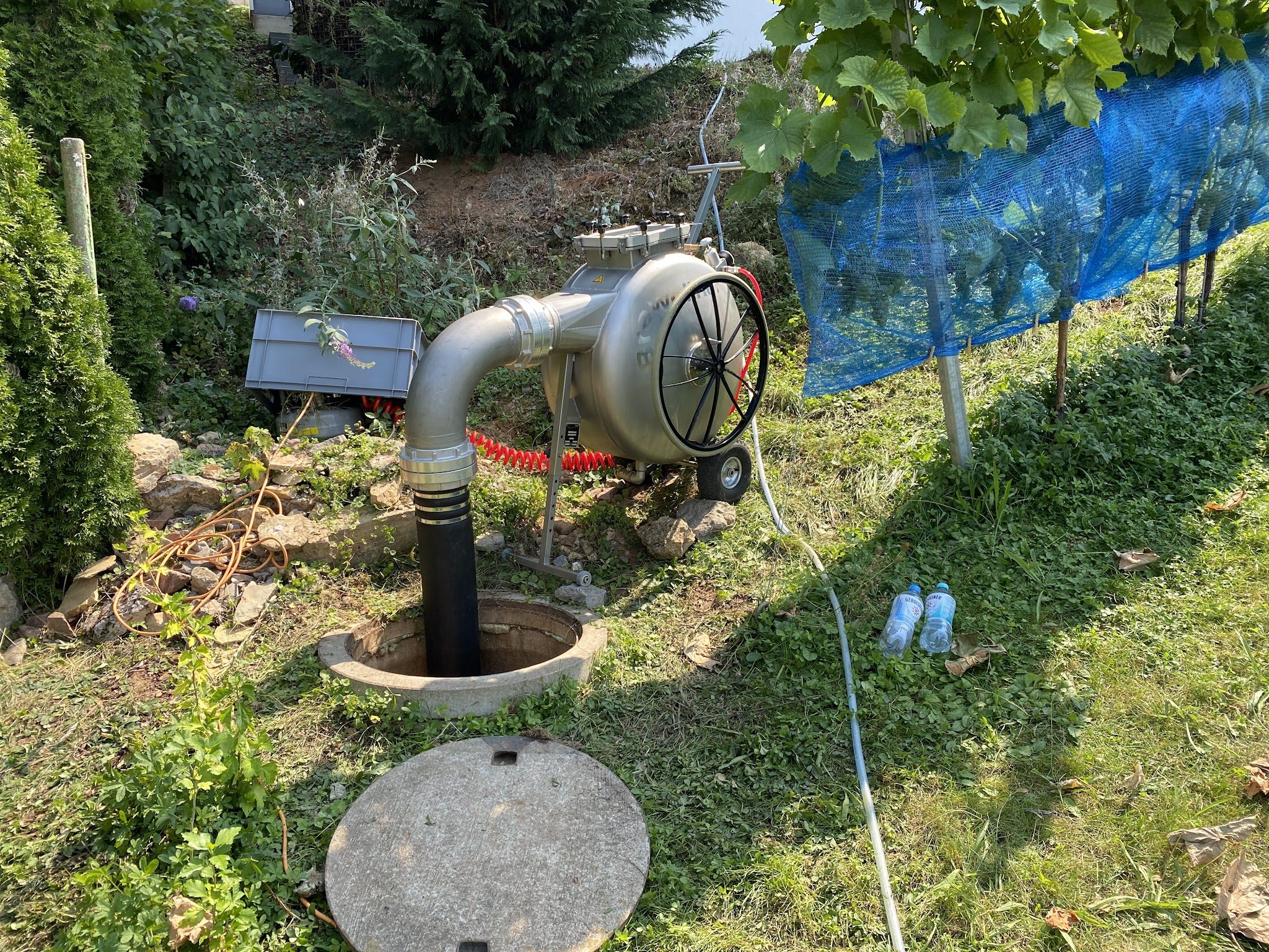 Gebläse und Schlauchtechnik an einem Schacht im Garten